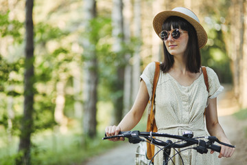 Naklejka premium Outdoor portrait of attractive young brunette in a hat on a bicycle.
