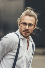 Close-up portrait of handsome stylish young man in spectacles and suspenders looking away