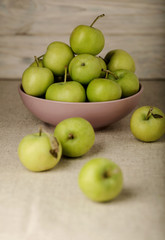 Green apples in a lilac plate on a wooden light background.