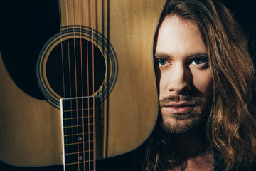 Close-up portrait of handsome bearded long haired man holding guitar and looking at camera