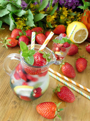 Refreshing drink with ice cubes, strawberries and mint in a glass jug