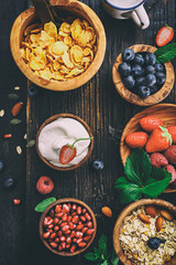 Healthy classic breakfast with oatmeal, cornflakes and various fresh berries on a black wooden surface. Toned.