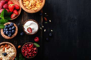 Healthy classic breakfast with oatmeal, cornflakes and various fresh berries on a black wooden surface.