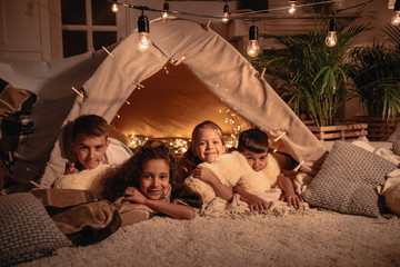 multiethnic group of children resting in handmade tent together at home