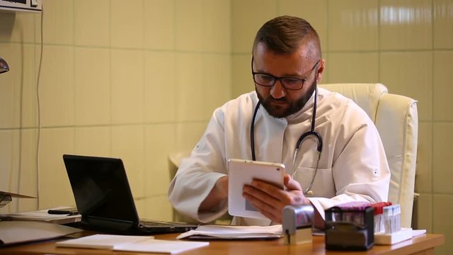 Absorbed doctor sitting in the office and working on modern technologies
