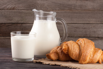 jug and glass of milk with croissants on a wooden background