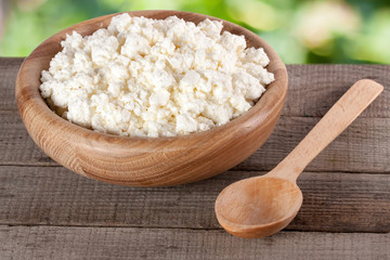Cottage cheese in a wooden bowl on board with blurred garden background