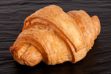 one croissant on black stone background closeup