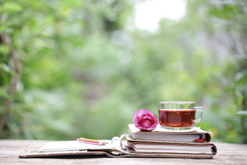 Tea in glass and notebook with flower on wooden table at outside