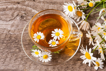 Herbal tea with fresh chamomile flowers on old wooden background