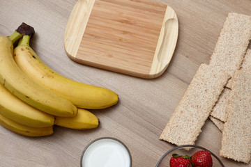 View from above. Healthy food. On a wooden table lie strawberries, bananas, bread and milk in a glass. Wooden background. Fruit on the table. Wooden board for text.