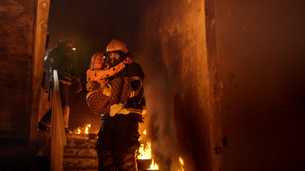 Fototapeta premium Brave Fireman Descends Stairs of a Burning Building with a Saved Girl in His Arms.