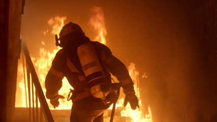 Naklejka premium Brave Firefighter Runs Up The Stairs. Raging Fire is Seen Everywhere.