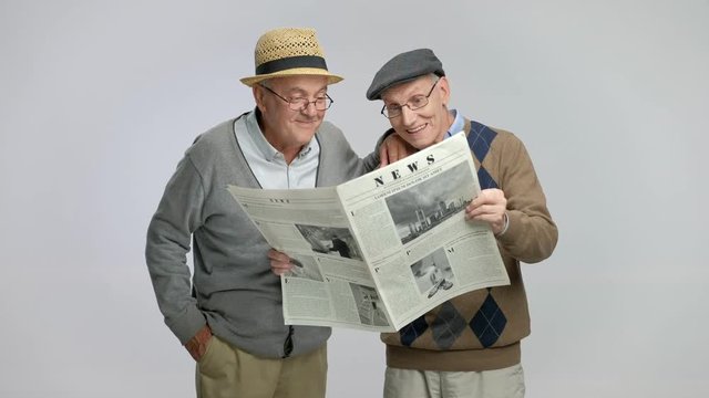 Two elderly men reading a newspaper and talking