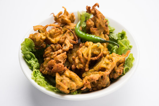 Crispy onion bhajis or kanda or pyaj ke pakore or pakoda , delicisous indian and brazilian street food on salad, typically enjoyed in rainy / monsoon season with hot tea, selective focus

