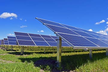 Solar panels on field. Clear sky with a few small clouds on background. 