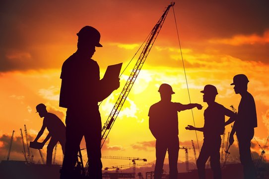 Silhouettes of workers working on construction site at suset.