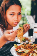 Young asian woman at the restaurant eating stir fry rice noodle with meat and vegetables,...