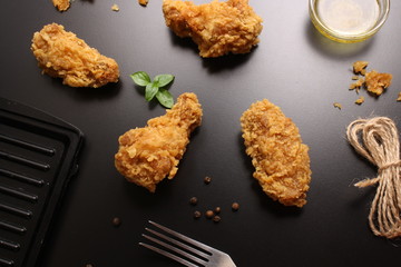 Wings of chicken in breading on a black background, butter and basil