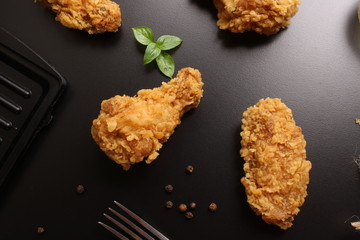 Wings of chicken in breading on a black background, butter and basil