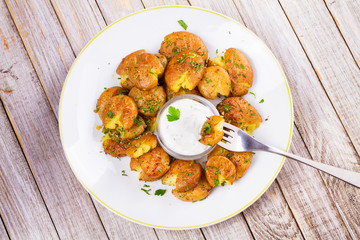 Smashed Potatoes with parsley, dried rosemary, lemon zest and yogurt sauce. View from above, top studio shot