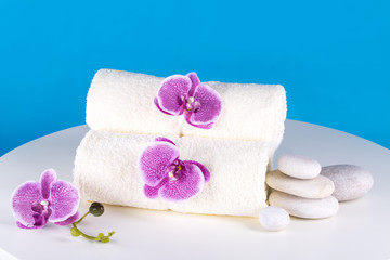 Spa. White towels, stones and orchids lie on the table, against the blue sky.