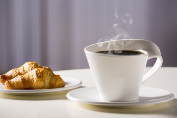White cup with coffee and croissants