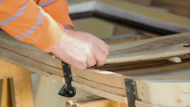 A joiner is putting on a wooden palet and he is adjusting it with a screw and automatic screwdriver. 