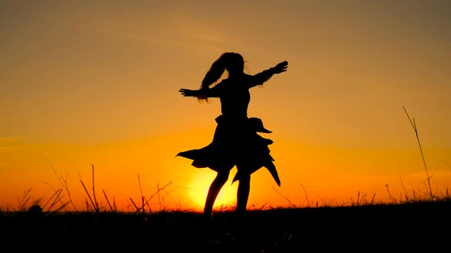 Silhouette of young witch dancing at field