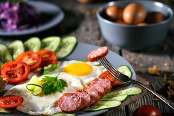 Fried eggs with vegetables and sausage on a wooden table