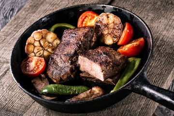 Juicy steak with vegetable garnish on an old frying pan