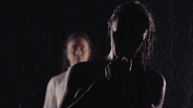 silhouette in the dark girl's thoughts, she stands naked in the rain. in the background her other half. they had a fight, but ready each other to forgive