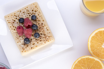 Crumpet topped with fruit on a white plate with orange juice and an orange cut in half 