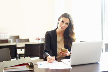 Working hard in the office. Shot of a young financial consultant doing some paperwork and text messaging while sitting at office desk.