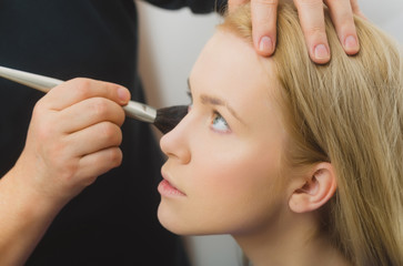 Hand of visagiste applying powder on girl face with brush