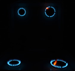 burning gas stove hob blue flames close up in the dark with reflection in mirror on a black background