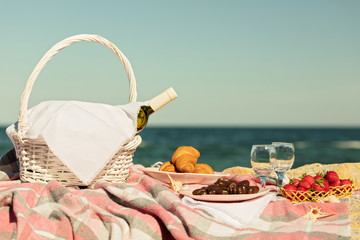 Summer time at the sea. Romantic picnic on the beach - wine, strawberries and sweets.
