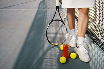 Tennis concept , woman legs next to tennis balls and refreshing drink next to net ; copy space ,...