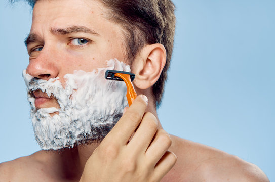 Young guy with a beard on a blue background in shaving foam