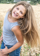 sexy little girl playing with her long hair posing in wheat field at a summer day