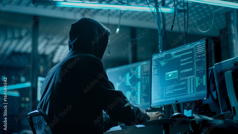 Poster shot from the back to hooded hacker breaking into corporate data servers from his underground hideou