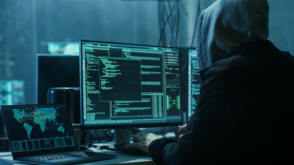 Dangerous Hooded Hacker Breaks into Government Data Servers and Infects Their System with a Virus. His Hideout Place has Dark Atmosphere, Multiple Displays, Cables Everywhere. - obrazy, fototapety, plakaty