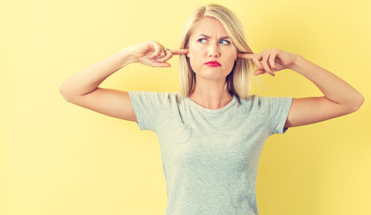 Young woman blocking her ears on a yellow background