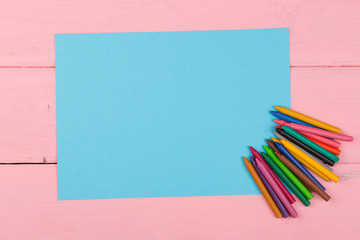 Blank blue paper and crayons on pink wooden table