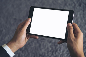 Mockup image of a business man sitting and holding black tablet pc with blank white screen with gray rug in background