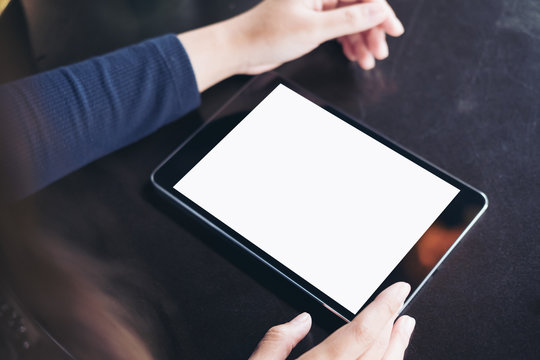 Mockup image of hands using a black tablet pc with blank white screen on vintage black table background