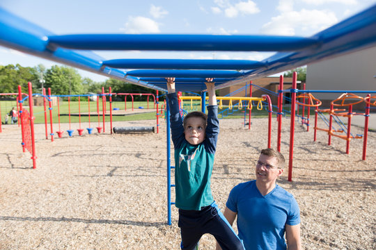 Boy swinging on monkey bars at playground, father watching him