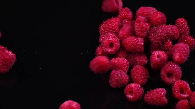 Fresh juicy raspberries falling on black background in slow motion. Shooting with high-speed camera
