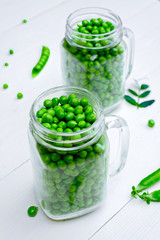 Full glass jar with fresh green peas on white wooden background. Bio healthy food. Green peas in jar, pods and pea leaves on wooden table