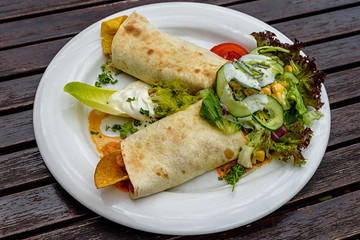 Burrito with sauce and vegetables on a white plate. Authentic mexican food. Top view